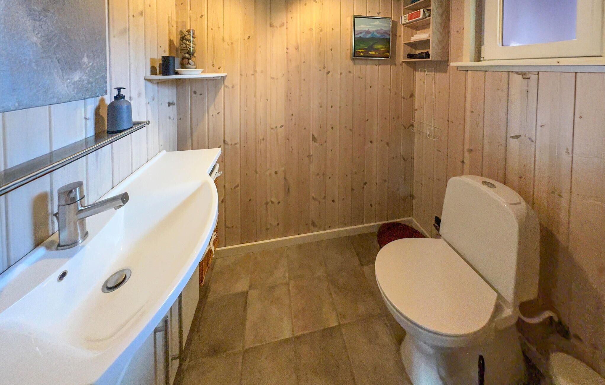 Een kleine badkamer met een wit wastafel, toilet en een plank met toiletartikelen.