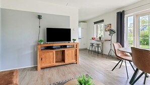 A modern living room with a flat-screen TV on a wooden stand, a dining area with a table and chairs, and a kitchen in the background. - Beautiful home in Paasloo with sauna (Paasloo)