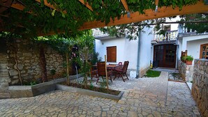 A stone-tiled patio with a wooden pergola, a table with chairs, and a small garden area. - House with heated pool (Bribir)