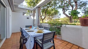 Un patio al aire libre con una mesa lista para comer, rodeada de sillas y una estructura blanca en el techo.
