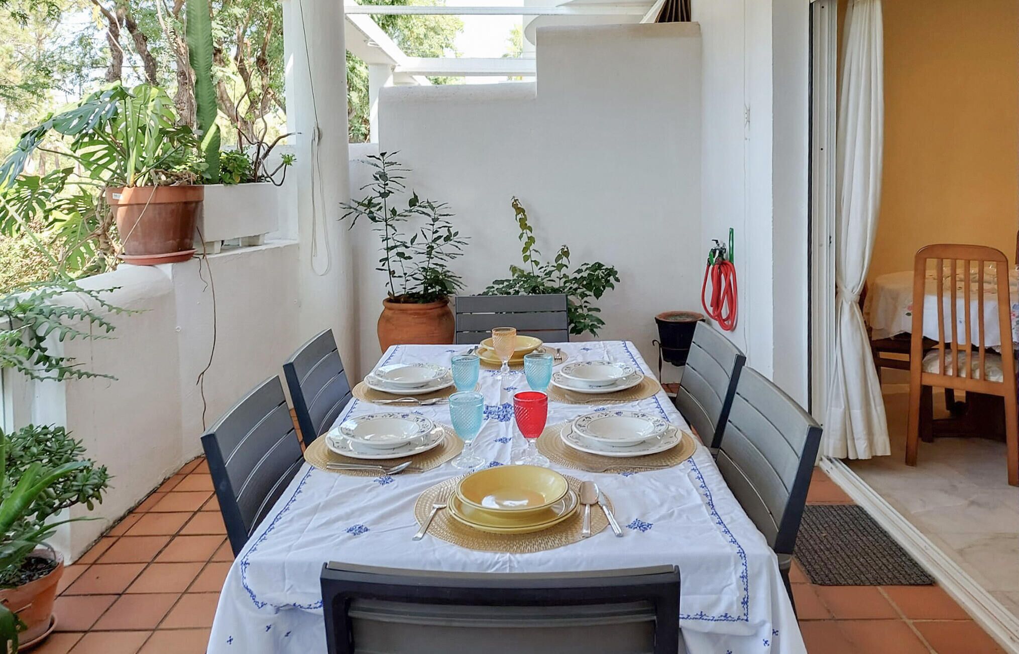 A patio table set for dining with a white tablecloth, blue floral pattern, and multiple plates, glasses, and cutlery.