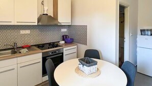 Una cocina compacta con armarios blancos, una estufa a gas, un lavamanos y una pequeña mesa de comedor con sillas.