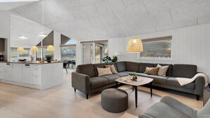 Ein modernes Wohnzimmer mit Küche, einem grauen Ecksofa, einem runden Hocker und Pendelleuchten.