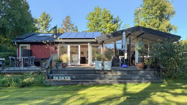 Een huis met een overdekte veranda, zonnepanelen en een tuin.