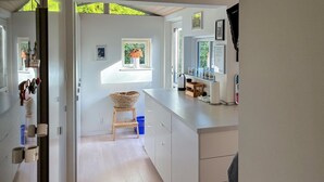 Een lichte keuken met witte kastjes, een houten kruk en een raam met uitzicht op groen.