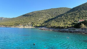 Una zona costera con agua turquesa cristalina, un litoral rocoso y colinas verdes al fondo.