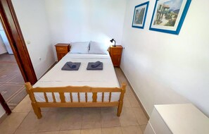 Ein Schlafzimmer mit einem hölzernen Bett, weißen Leinen, zwei Nachttischen, einer Lampe und zwei gerahmten Bildern an der Wand.