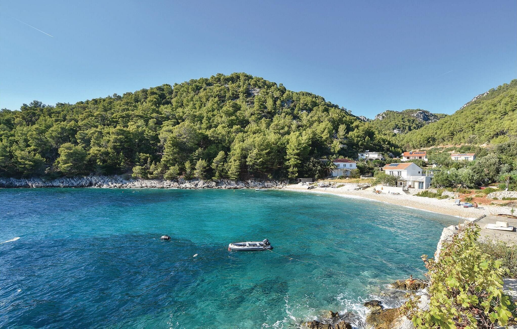 A coastal area with clear turquoise waters, a boat anchored near the shore, and buildings on the hillside.