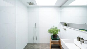 Een moderne badkamer met witte tegels, een douche, een wastafel met een groene kruk en een potplant.