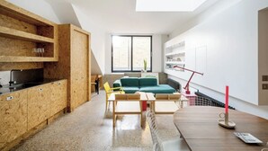 Een moderne keuken met houten keukenkastjes, een eethoek met een houten tafel en stoelen, een groene bank en een dakraam boven de keuken.
