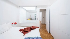 Een moderne slaapkamer met een groot bed, een rood-wit geruit plaid, een rode bolvormige decoratie aan de muur en een uitzicht op een andere kamer door een groot raam.