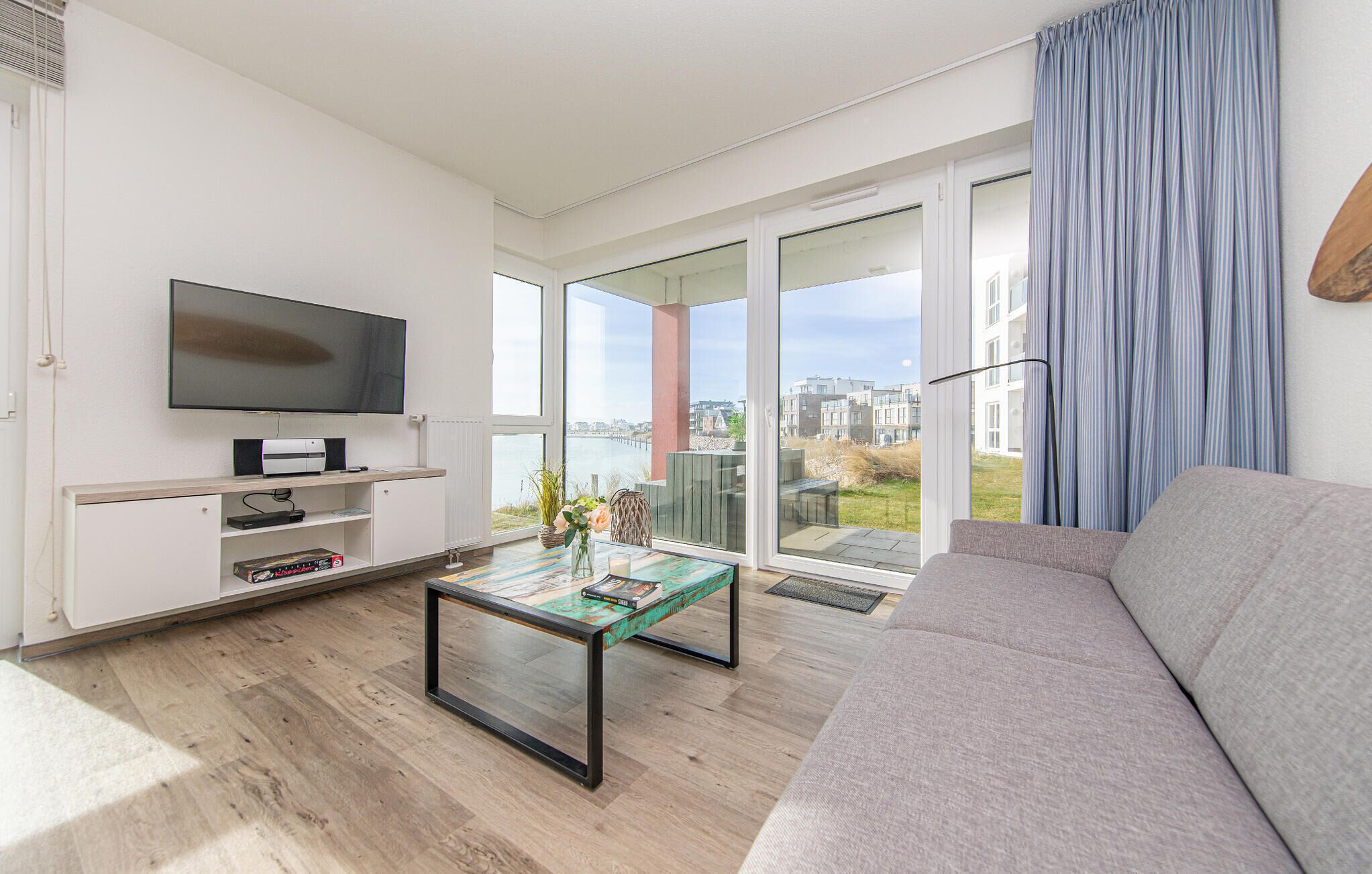 A modern living room with a flat-screen TV, a sofa, a coffee table, and a view of the city through large windows.