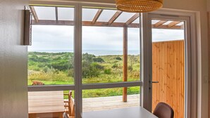 Una habitación con puertas de vidrio grandes que dan a una terraza exterior con vista al mar y follaje.