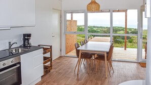 Una cocina moderna con cafetera, un comedor con mesa y sillas, y ventanas amplias que ofrecen vistas al paisaje.