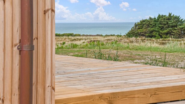 Una terraza de madera que da a una playa, con vista clara al océano y una zona boscosa.