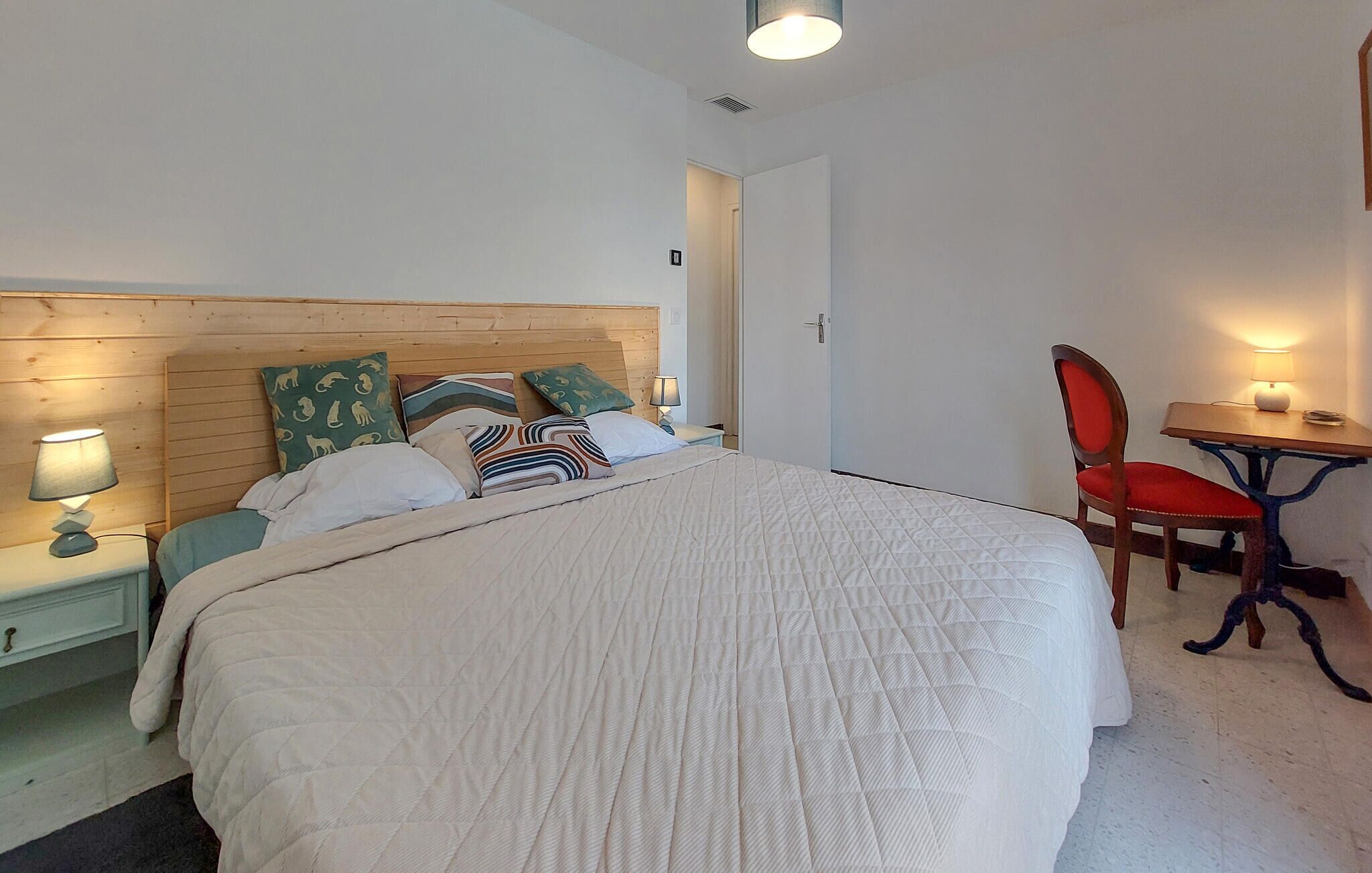 Een netjes ingerichte slaapkamer met een bed, nachtkastjes, een stoel en een tafeltje met een lamp.