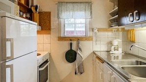 A compact kitchen with white appliances, a window with a patterned valance, and a hanging pot holder. - 3 bedroom beautiful home in Torsby (Torsby)