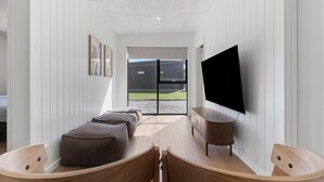 Un interior moderno con sofá, sillas de madera, televisor y vistas a través de un ventanal.