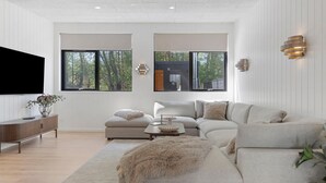 Una sala de estar moderna con sofá, reposapiés y televisor de pantalla plana.