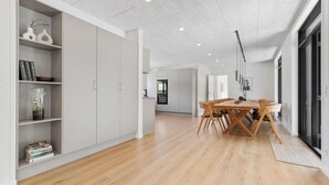 Un interior moderno con una mesa de comedor de madera, muebles de cocina blancos y una zona de cocina.