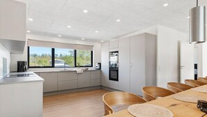 Una cocina moderna con horno empotrado, cafetera y ventana con vistas a la vegetación.