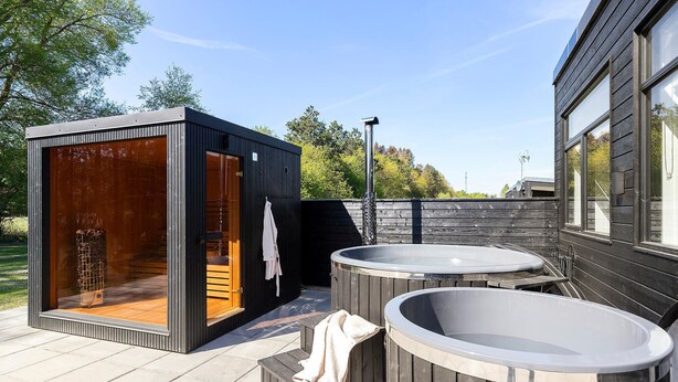 Un moderno espacio exterior con spa, que incluye una sauna de madera, un jacuzzi y una sala con paredes de vidrio.