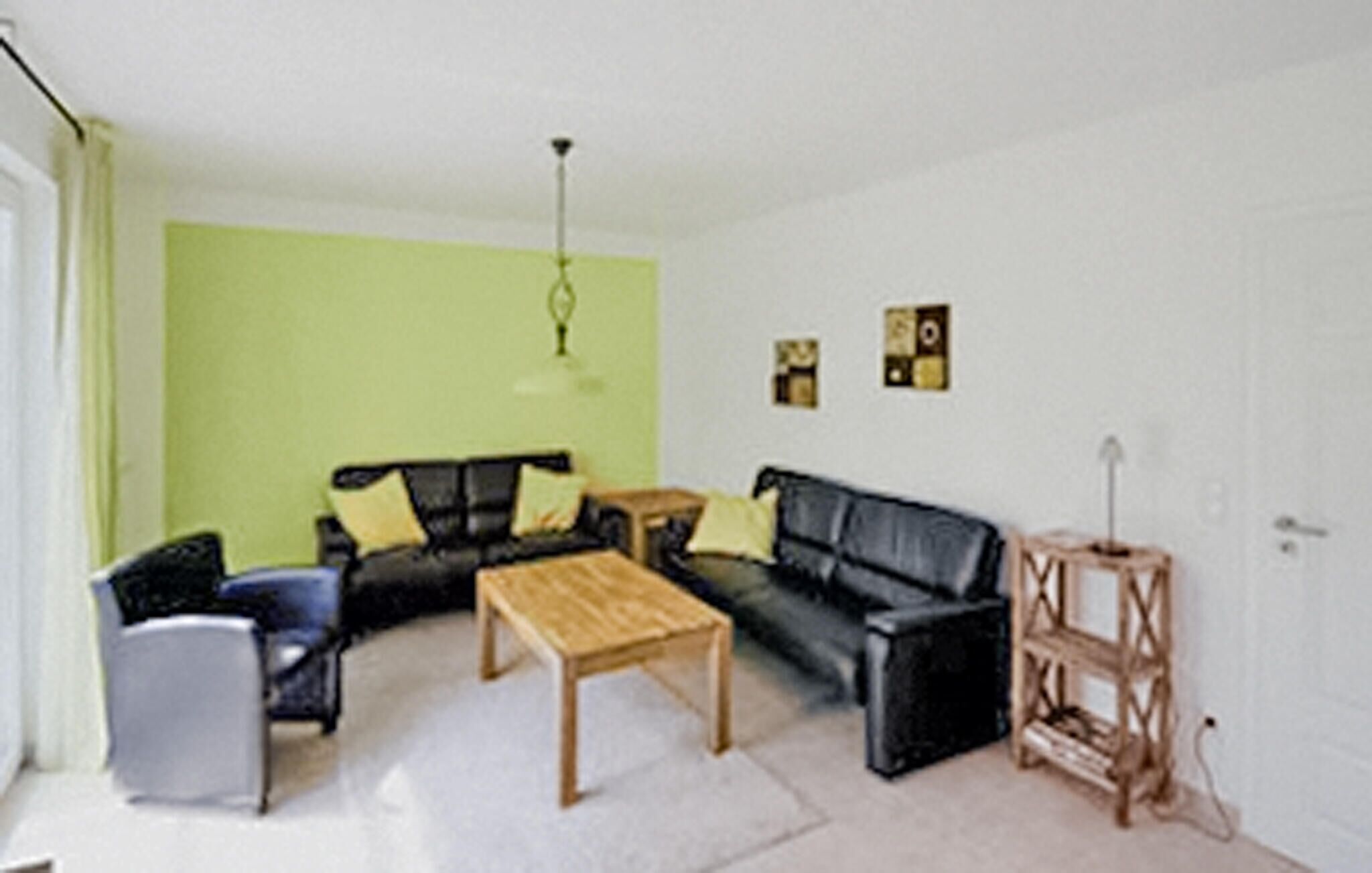 A living room with a black sofa, a wooden coffee table, and a grey armchair. There is a green accent wall and a small wooden side table.