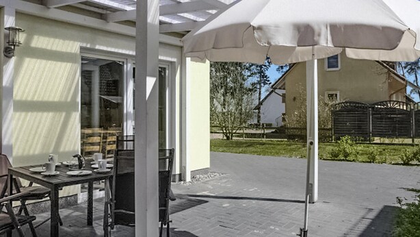 Un espace extérieur aménagé en terrasse, avec une table dressée pour les repas, un parasol blanc et un coin salon abrité.