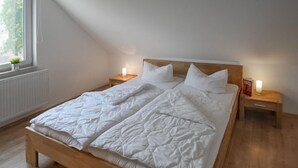 Une chambre à coucher avec un lit en bois, du linge de lit blanc, deux tables de chevet avec des lampes et une fenêtre donnant sur un paysage verdoyant.