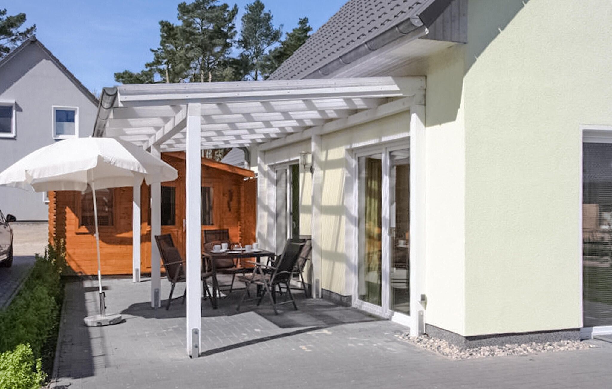 A covered patio with a table and chairs, a white umbrella, and a wooden deck.