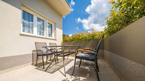 An outdoor patio with a table and chairs, a window, and a wall with greenery. - Nice apartment in Podstrana with WiFi (Podstrana)