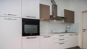 A modern kitchen with white cabinets, a black oven, a stainless steel range hood, a sink, and a door. - Nice apartment in Podstrana with WiFi (Podstrana)
