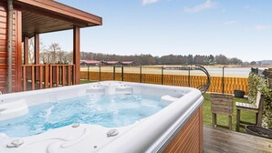 Ein Whirlpool auf einer Holzterrasse mit Blick auf einen eingezäunten Bereich und Gebäude im Hintergrund.