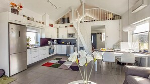 Una cucina moderna con mobili bianchi, un'area pranzo con tavolo e sedie, e una scala che conduce a un piano superiore.