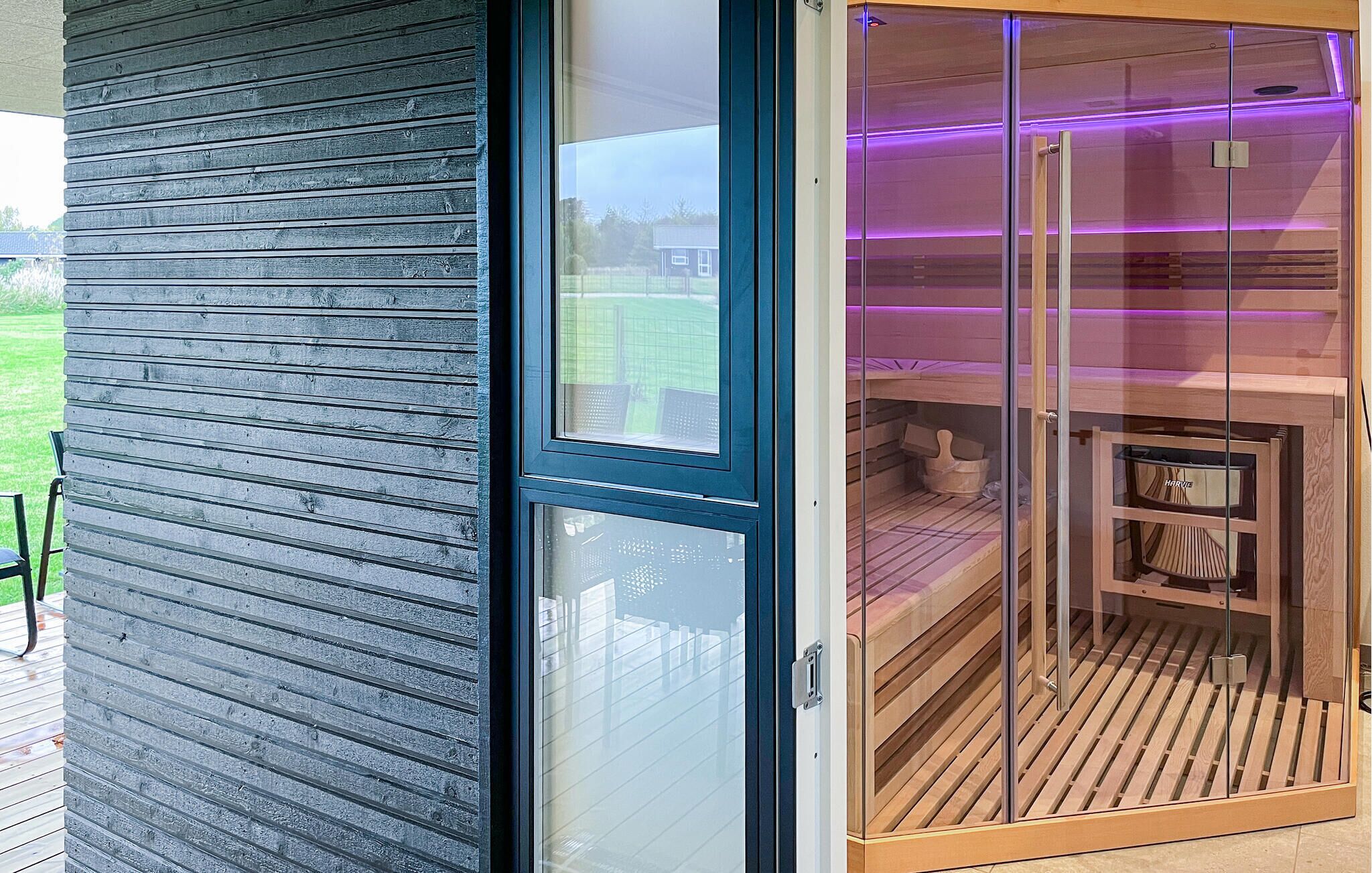 A sauna with a glass door, wooden benches, and a purple light strip.