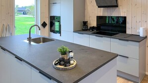 Une cuisine moderne dotée d’un grand îlot central, d’appareils électroménagers en acier inoxydable et offrant une vue sur un paysage verdoyant.