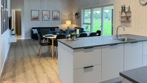 Une cuisine moderne dotée d’un îlot central, un coin repas avec une table et des chaises, et un espace de vie avec un canapé et des fauteuils.