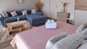 Ein modernes Schlafzimmer mit einem großen Bett, einem blauen Sofa, einem Holztischchen und einem kleinen Nachttisch mit einer Vase.