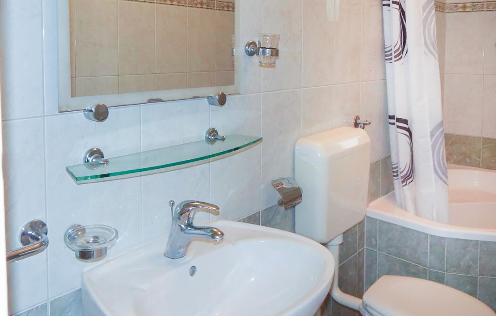 A bathroom with a white sink, a glass shelf, a toilet, and a shower curtain.