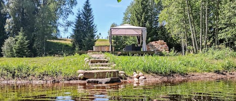 A gazebo with a clear view of a pond, surrounded by greenery and trees.