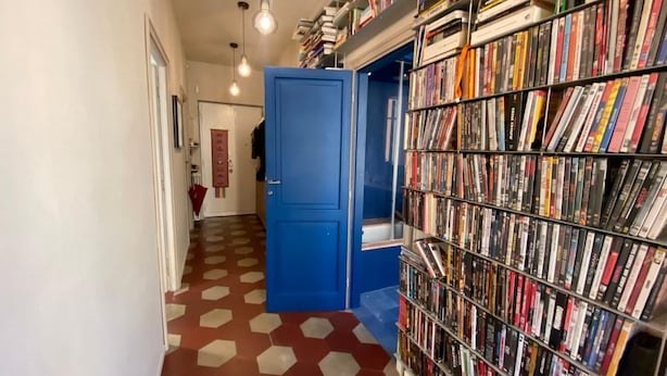 Ein Korridor mit einem gemusterten Boden, einer blauen Tür und einem Bücherregal voller Bücher.