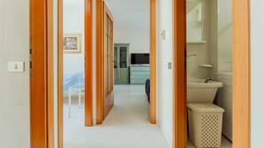 A hallway with wooden doors, a bed, a TV, a washing machine, and a laundry basket. - GuestHost - Spacious apartment of about 100 sqm, ideal for groups or families of up to 6 guests, located on the third floor of a building with an elevator (NOT for disabled persons). The property is situated in the residential district of La Vega, a quie (Cagliari)