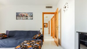A modern living room with a sofa, ottoman, and a painting of a cityscape. - GuestHost - Spacious apartment of about 100 sqm, ideal for groups or families of up to 6 guests, located on the third floor of a building with an elevator (NOT for disabled persons). The property is situated in the residential district of La Vega, a quie (Cagliari)