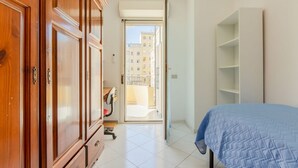A bedroom with a bed, a wardrobe, a desk, and a view through an open door. - GuestHost - Spacious apartment of about 100 sqm, ideal for groups or families of up to 6 guests, located on the third floor of a building with an elevator (NOT for disabled persons). The property is situated in the residential district of La Vega, a quie (Cagliari)