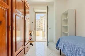 A bedroom with a bed, a wardrobe, a desk, and a view through an open door.
