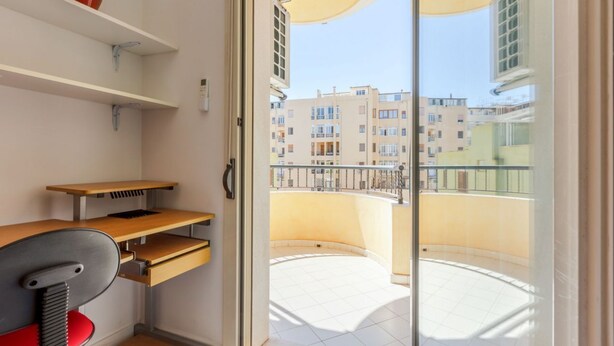 A room with a desk, chair, shelves, and a balcony with a view of buildings. - GuestHost - Spacious apartment of about 100 sqm, ideal for groups or families of up to 6 guests, located on the third floor of a building with an elevator (NOT for disabled persons). The property is situated in the residential district of La Vega, a quie (Cagliari)