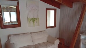 A white sofa in a room with wooden beams, a window, and a painting of a flower on the wall. - Apartment 'Casa Sabine' in Freiburg im Breisgau at Tuniberg with Mountain View and Wi-Fi (Freiburg)