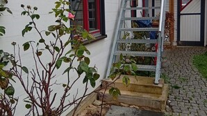A white building with a red-framed window, a metal staircase, and a small garden area with a rose bush. - Apartment 'Casa Sabine' in Freiburg im Breisgau at Tuniberg with Mountain View and Wi-Fi (Freiburg)