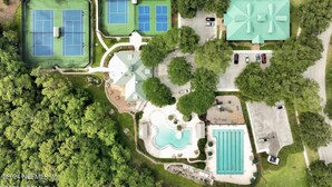 Ett flygbildsbild av en fastighet med flera tennisbanor, en swimmingpool och en stor byggnad med ett grönt tak.
