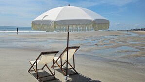 En strand med ett vitt parasoll och två strandstolar.